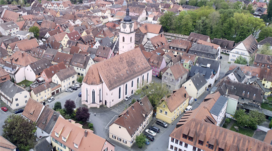 Farbiges Schrägluftbild einer Stadt, in der Mitte ist eine Kirche.